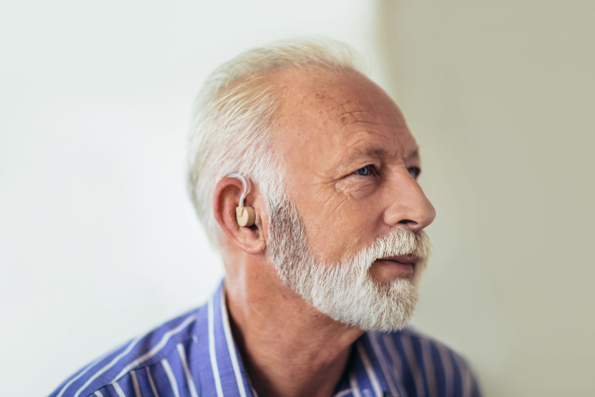 An older man with a beard is wearing a hearing aid in his ear.