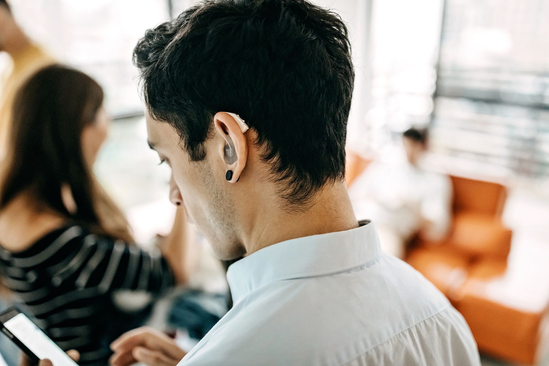 A man wearing a hearing aid is looking at his phone.