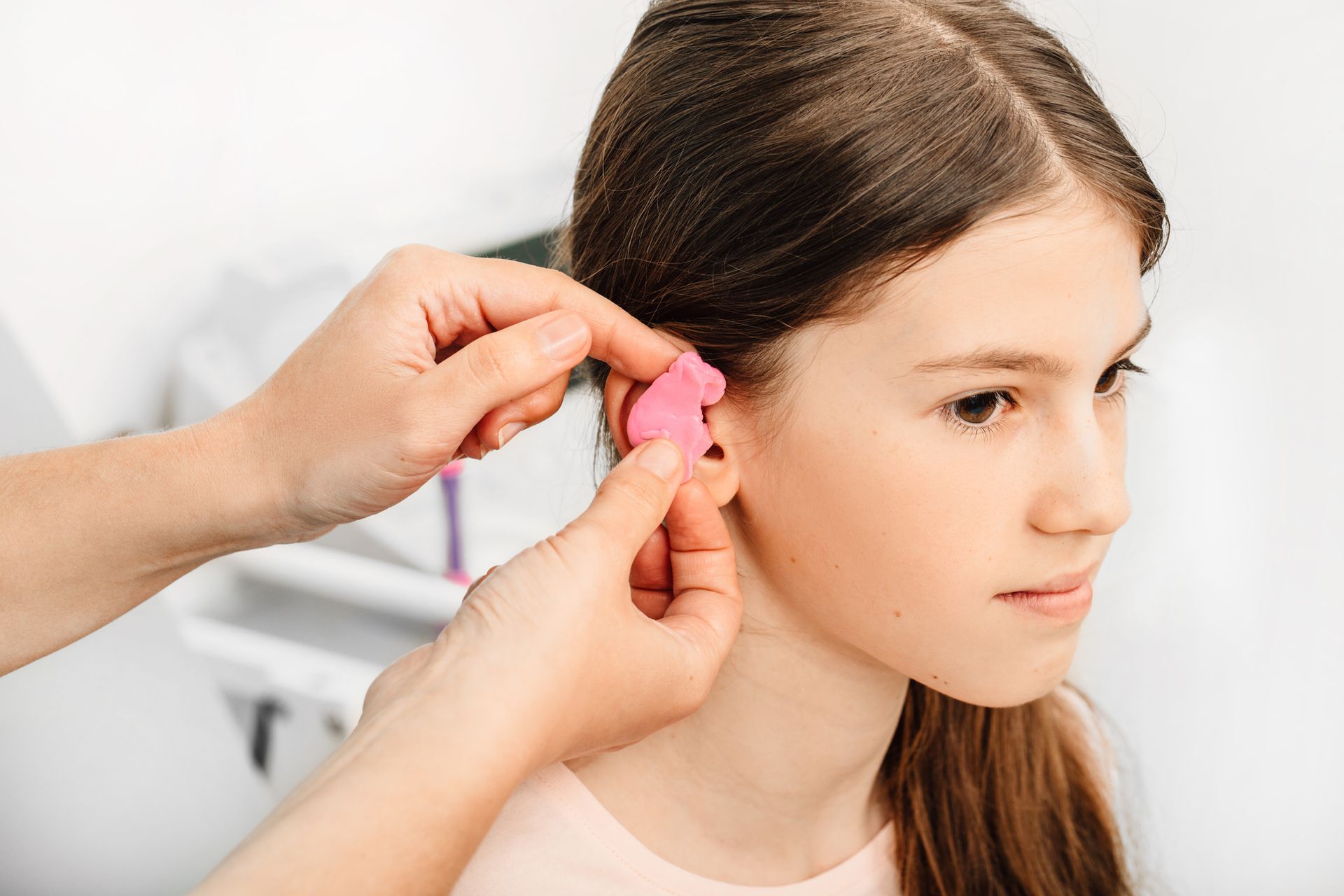 A woman is putting ear plugs in a young girl 's ear.