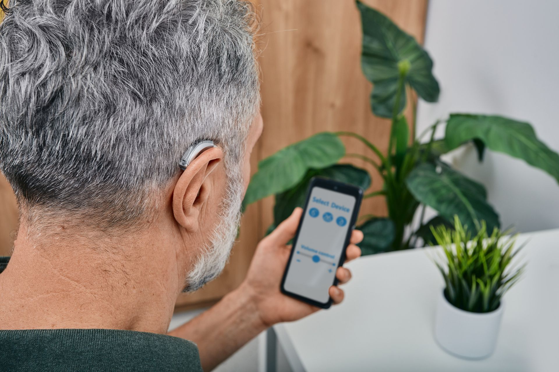 A man with a hearing aid is using a smart phone.