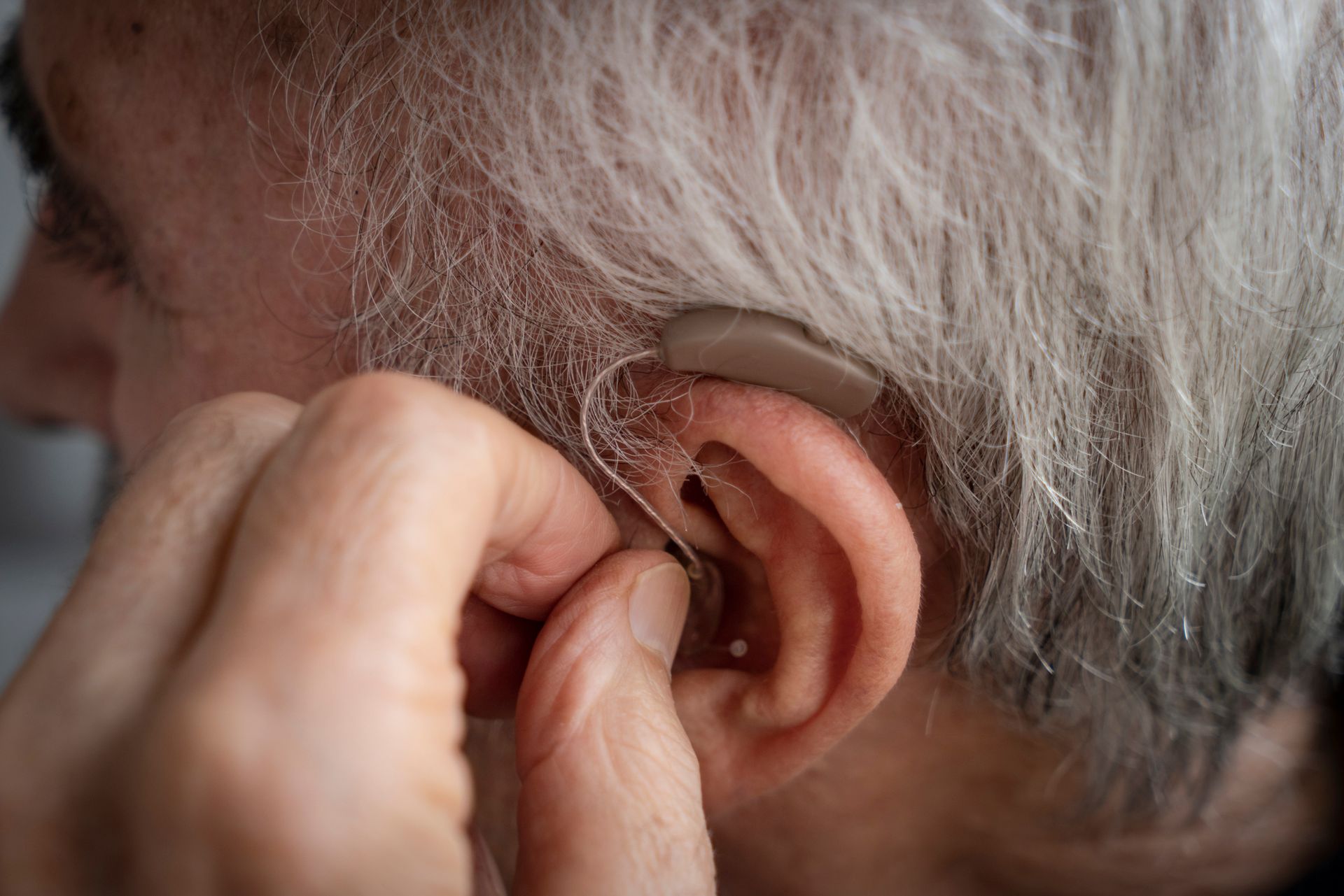 An elderly man is putting a hearing aid in his ear.