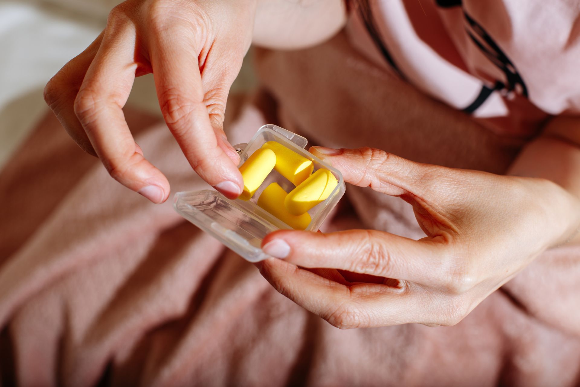 A woman is holding a pair of yellow ear plugs in her hands.