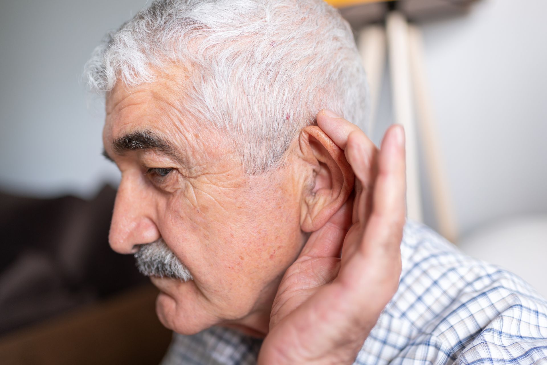 An elderly man is holding his hand to his ear.