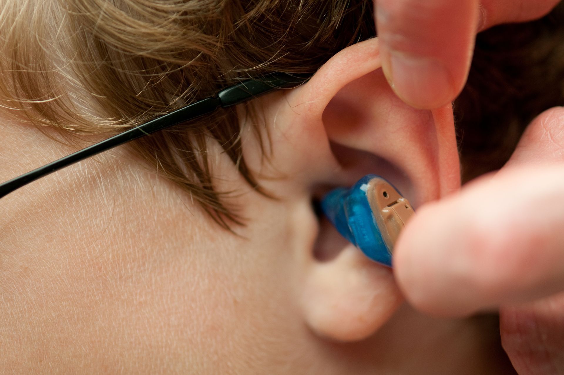 A person is putting a hearing aid in a child 's ear.