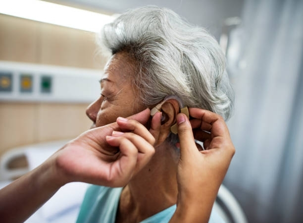 An elderly woman is getting a hearing aid in a hospital room.