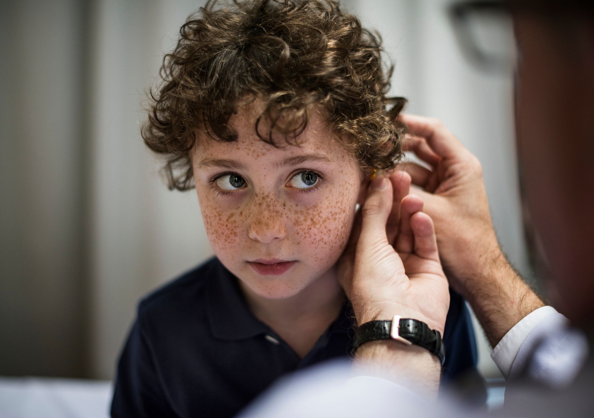 A young boy is getting his ears examined by a doctor.