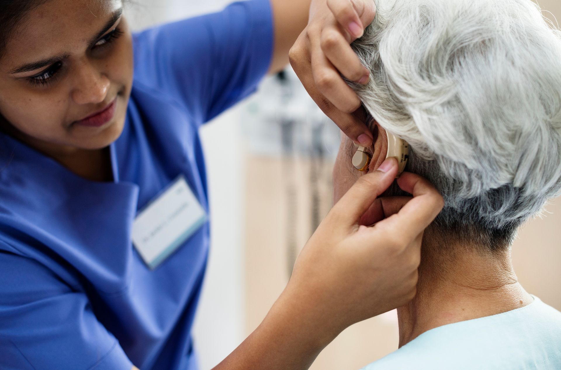 A nurse is putting a hearing aid in an older woman 's ear.