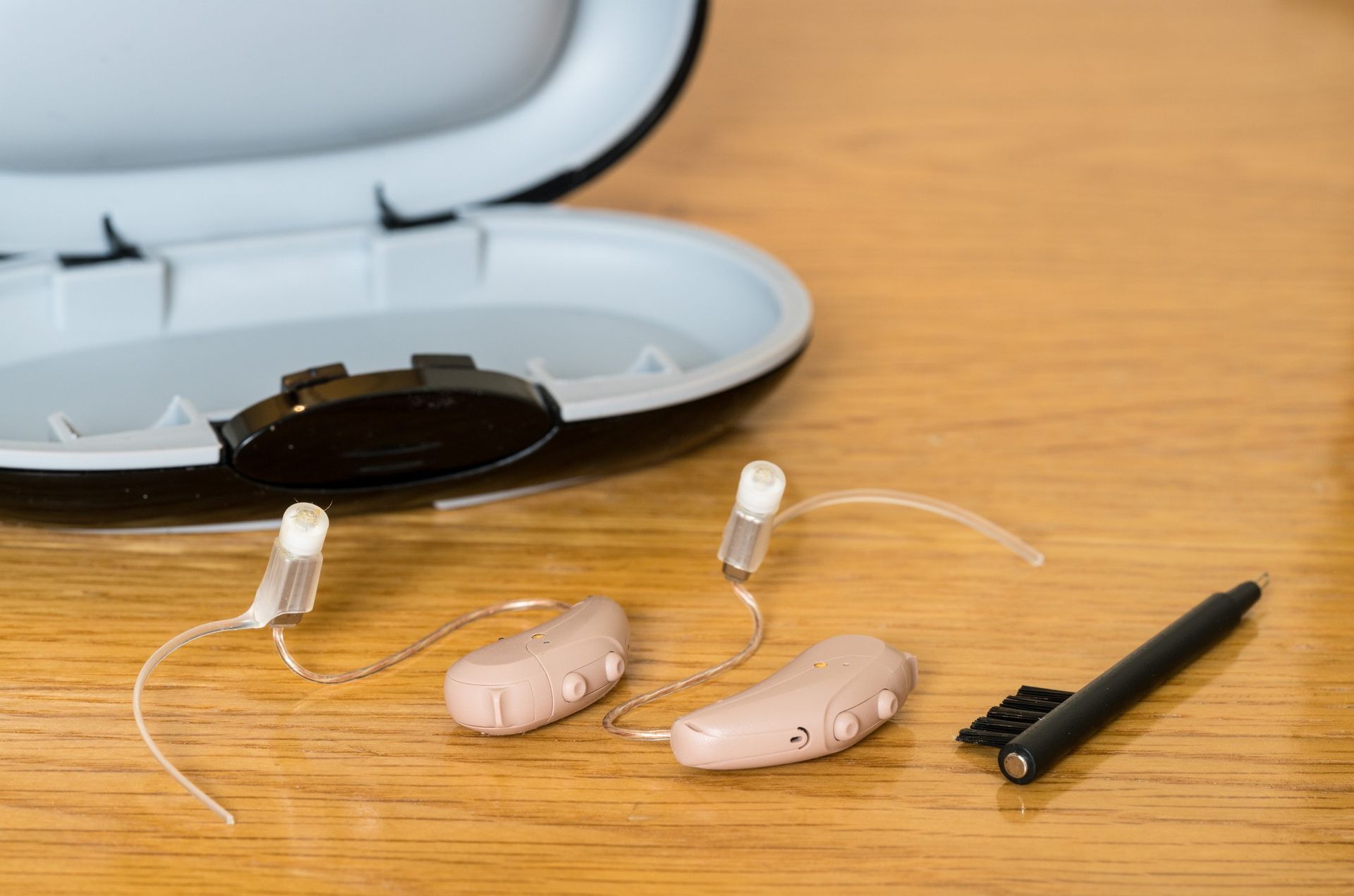 A pair of hearing aids are sitting on a wooden table next to a case.