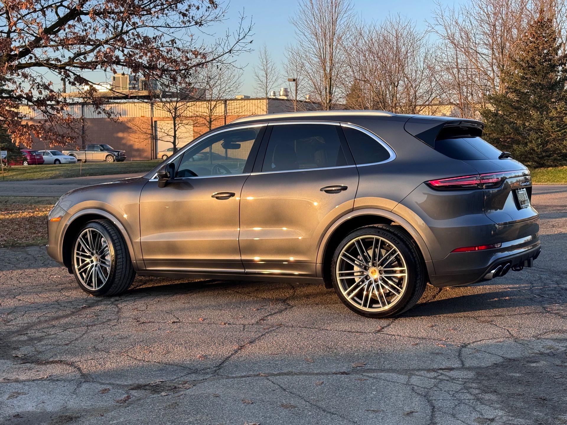 Gray Porsche SUV parked on asphalt. Trees and a brick building are in the background.