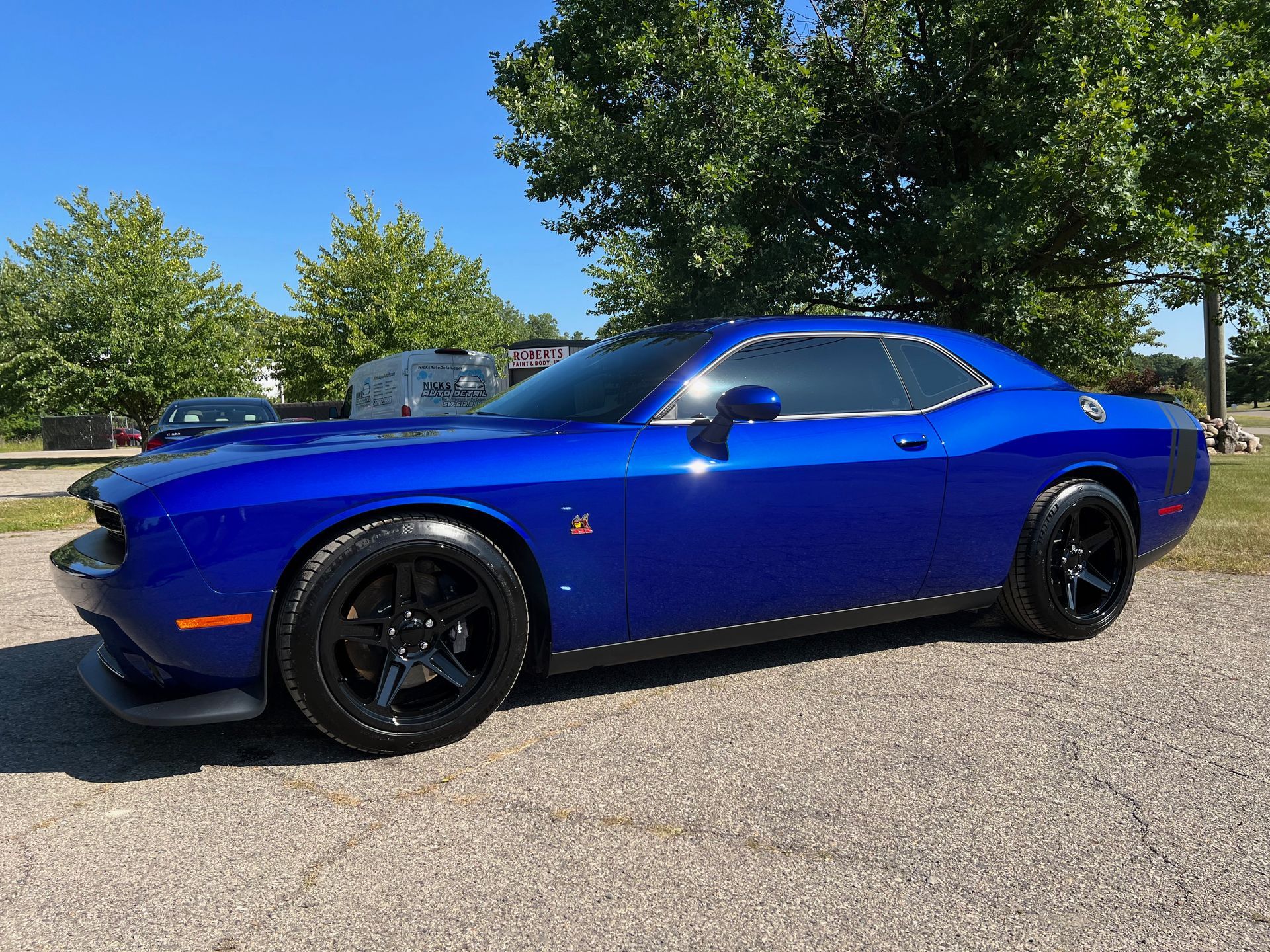 Blue Dodge Challenger parked on gravel, sunny day. Black wheels and trim.