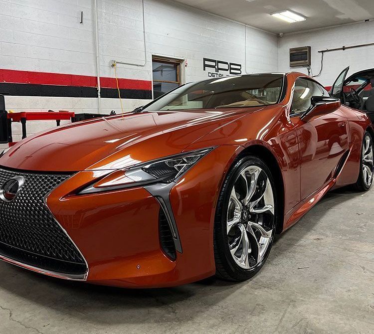 Orange Lexus LC coupe in a garage, shiny chrome wheels.