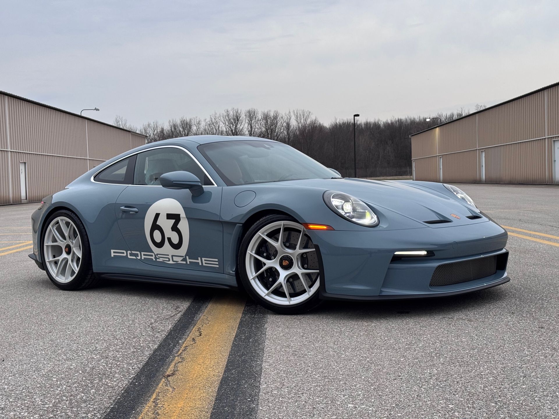Blue Porsche 911 coupe with racing livery, parked on asphalt.