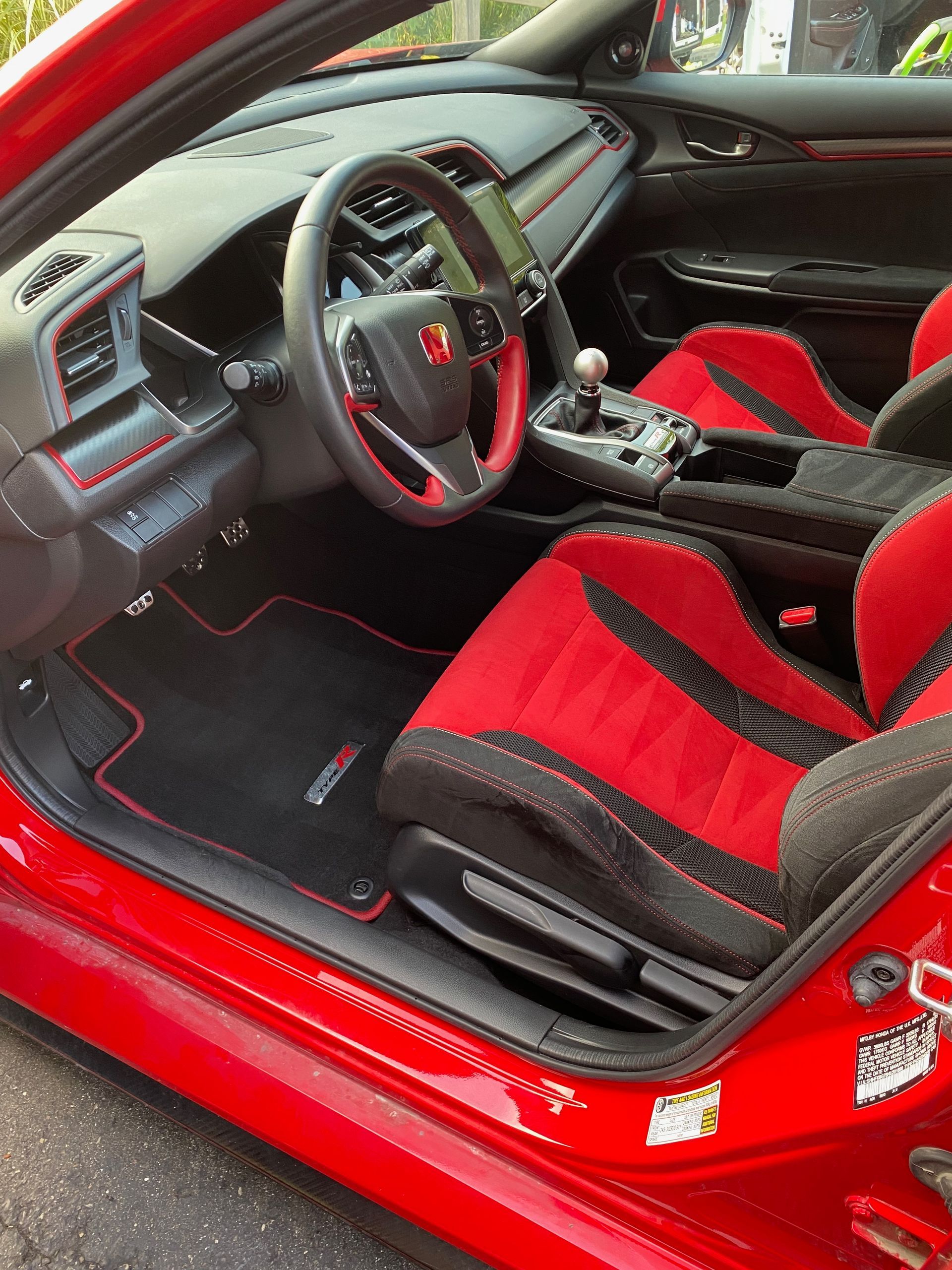 Red interior of a Honda Civic Type R. Red bucket seats, black accents, red stitching, and a manual transmission.