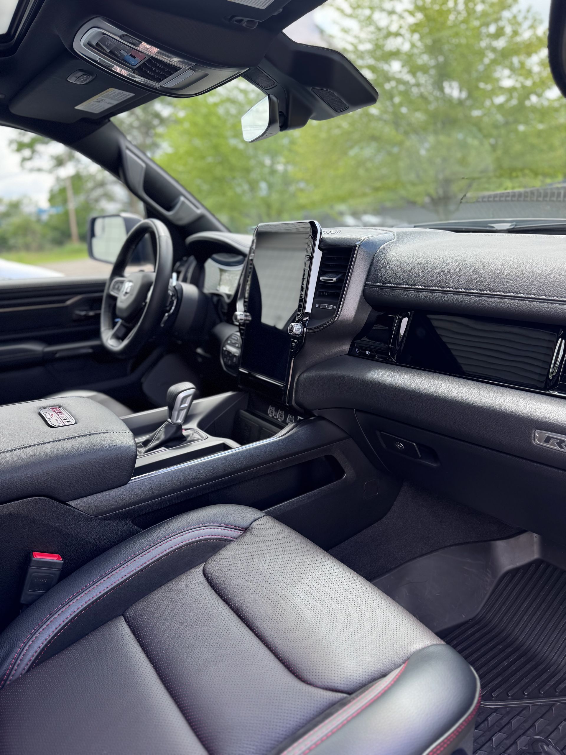 Interior view of a black truck. Seats, dashboard, steering wheel and infotainment screen are visible. Window view.