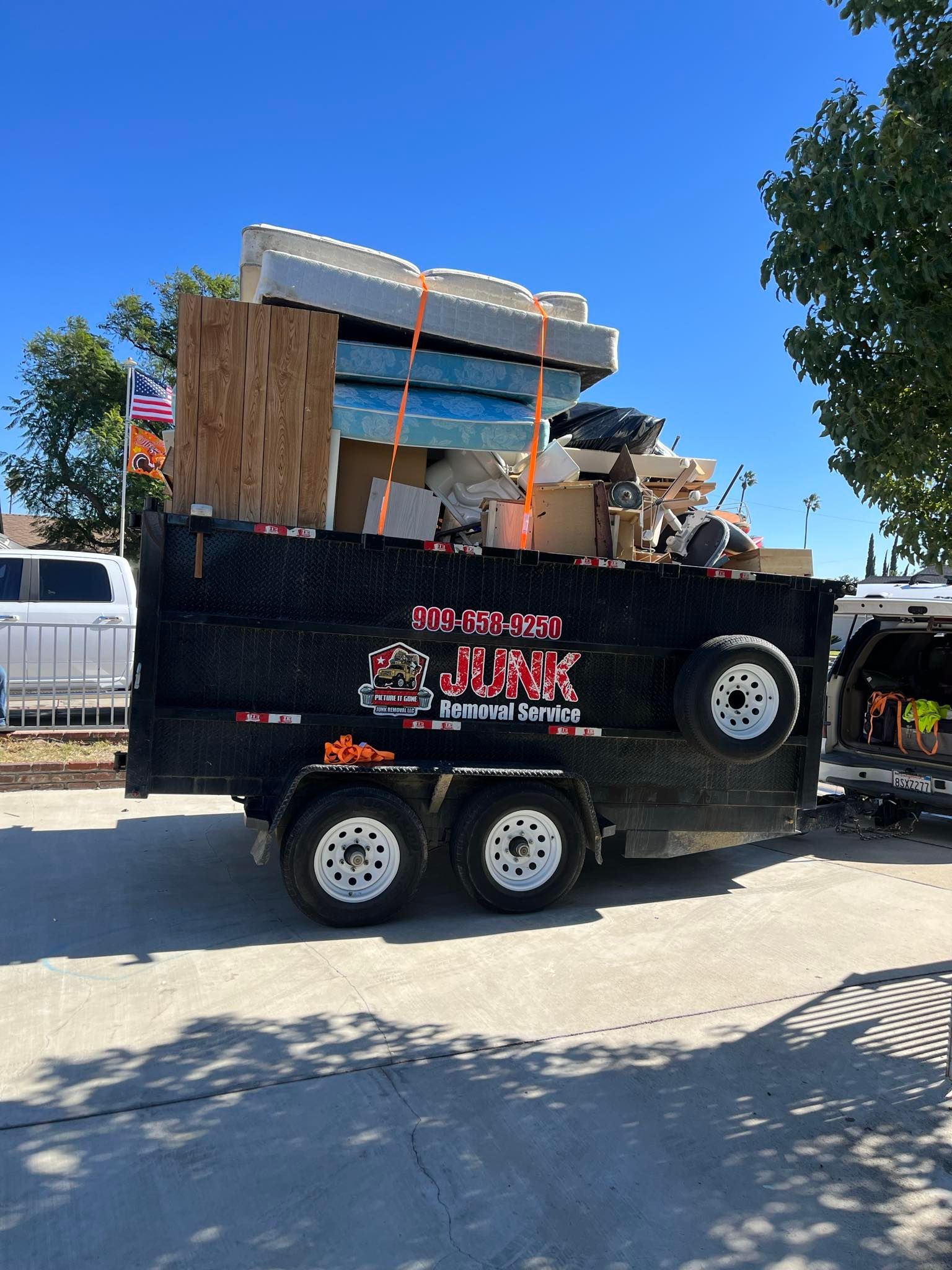 Black trailer loaded with debris and furniture; a sunny outdoor scene.