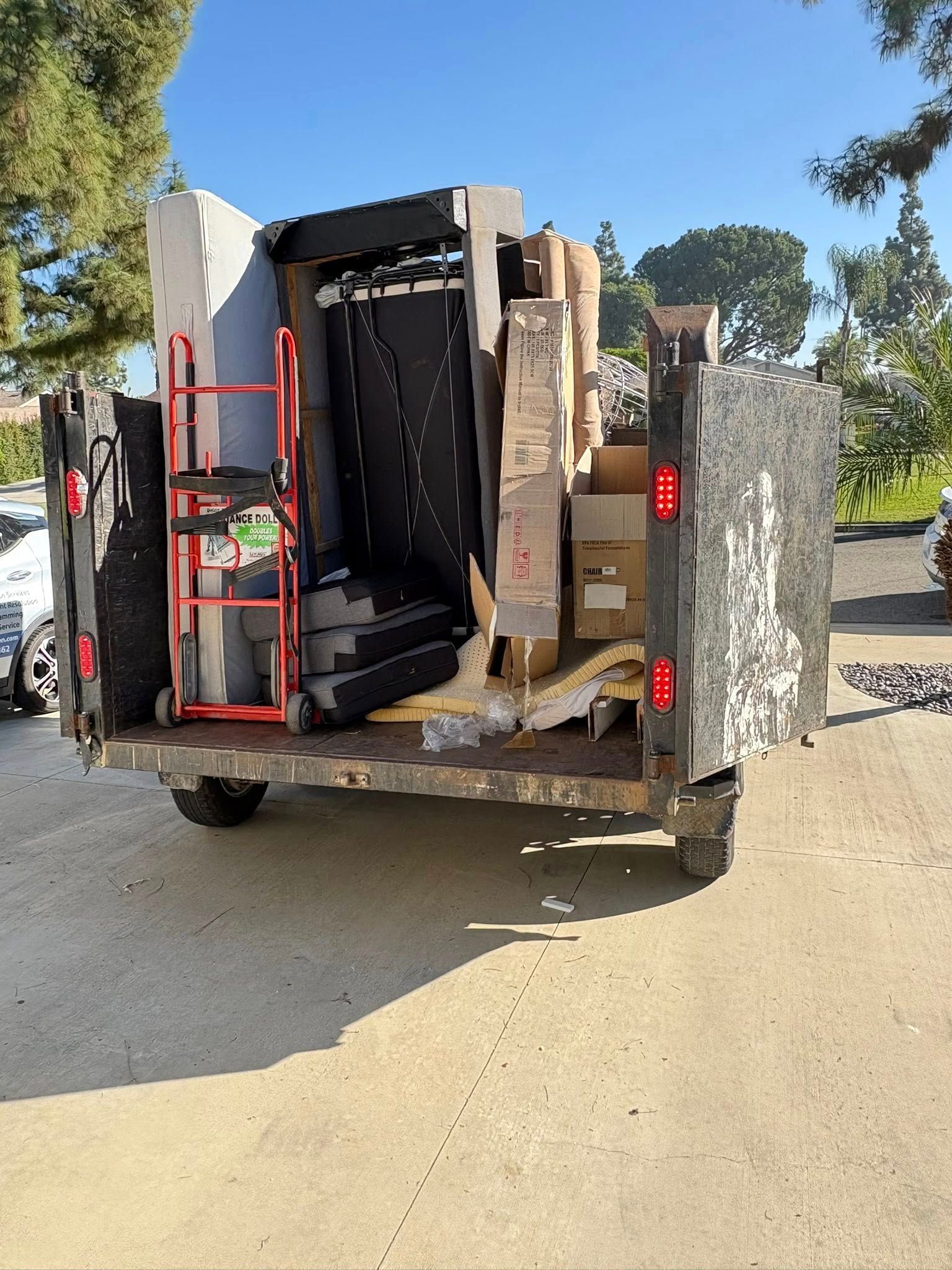 A truck bed overflowing with packed boxes and furniture, including a hand truck, on a sunny day.