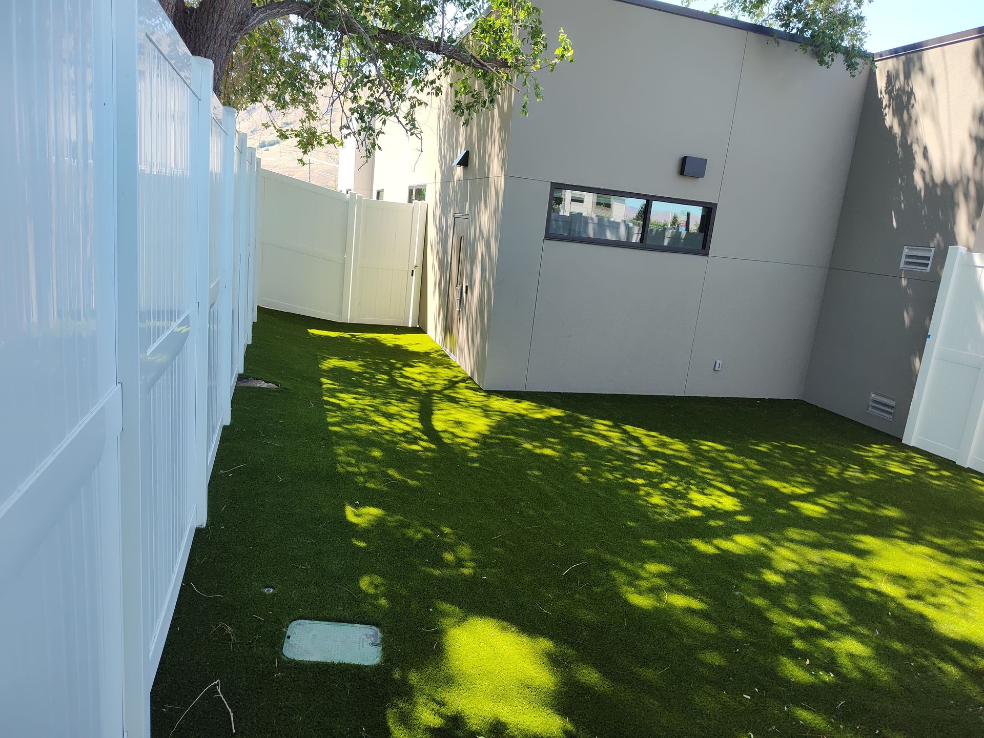 A backyard with a white fence and green grass.