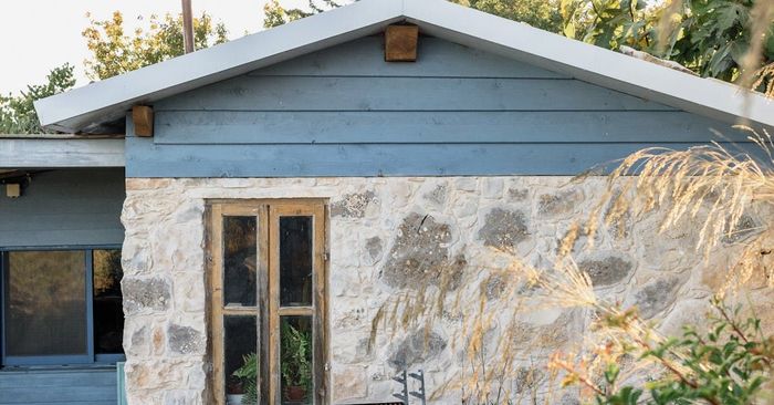 Stone cottage exterior with blue siding, wooden door, and natural landscaping.