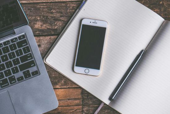 Laptop, smartphone, and notebook on a wooden desk, suggesting work or study.