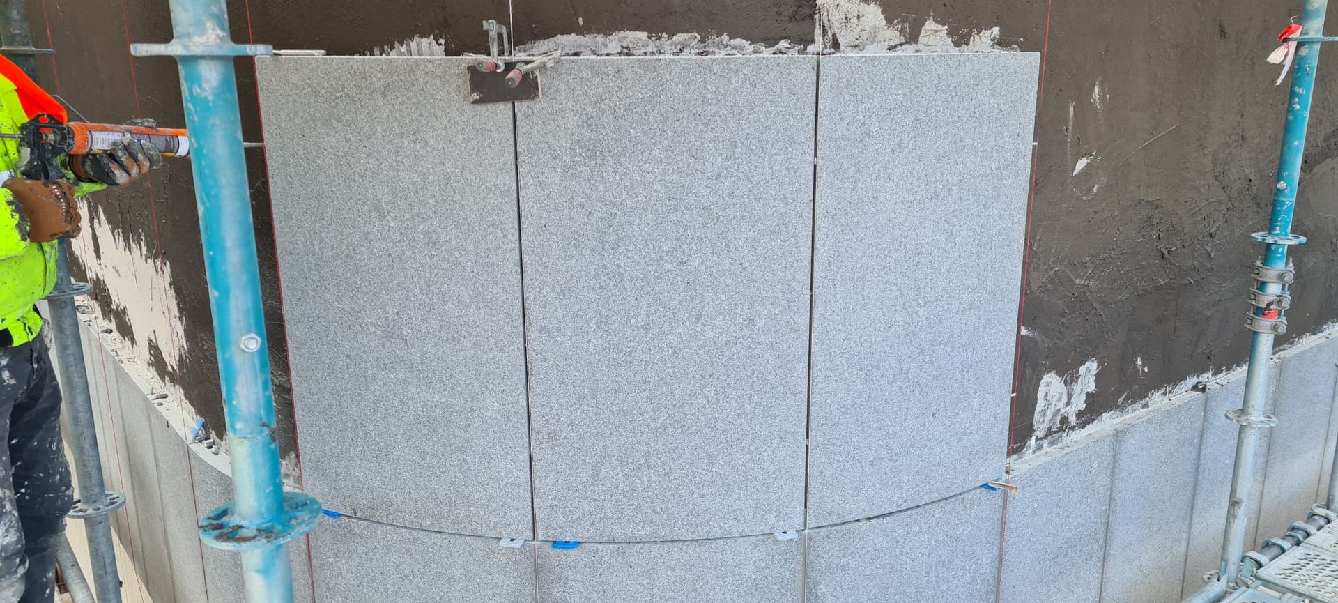 Een man installeert granieten tegels op de zijkant van een gebouw.