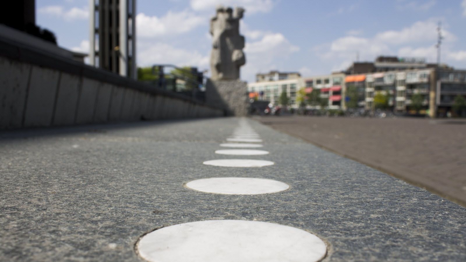 Een rij witte cirkels op een straat met een standbeeld op de achtergrond
