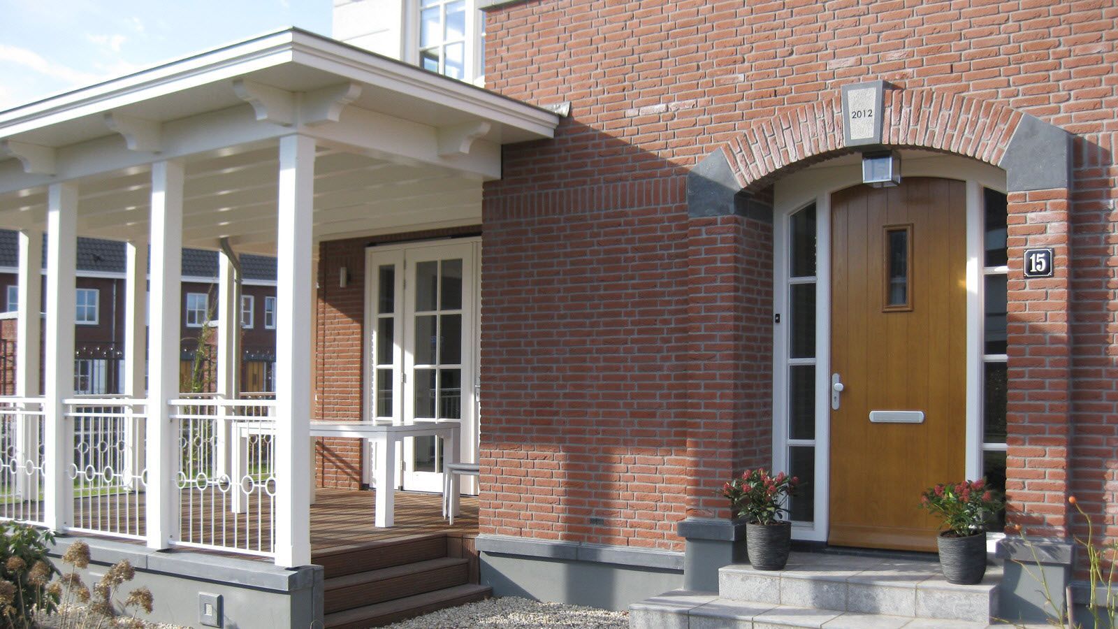 Een bakstenen huis met een veranda en een gele deur