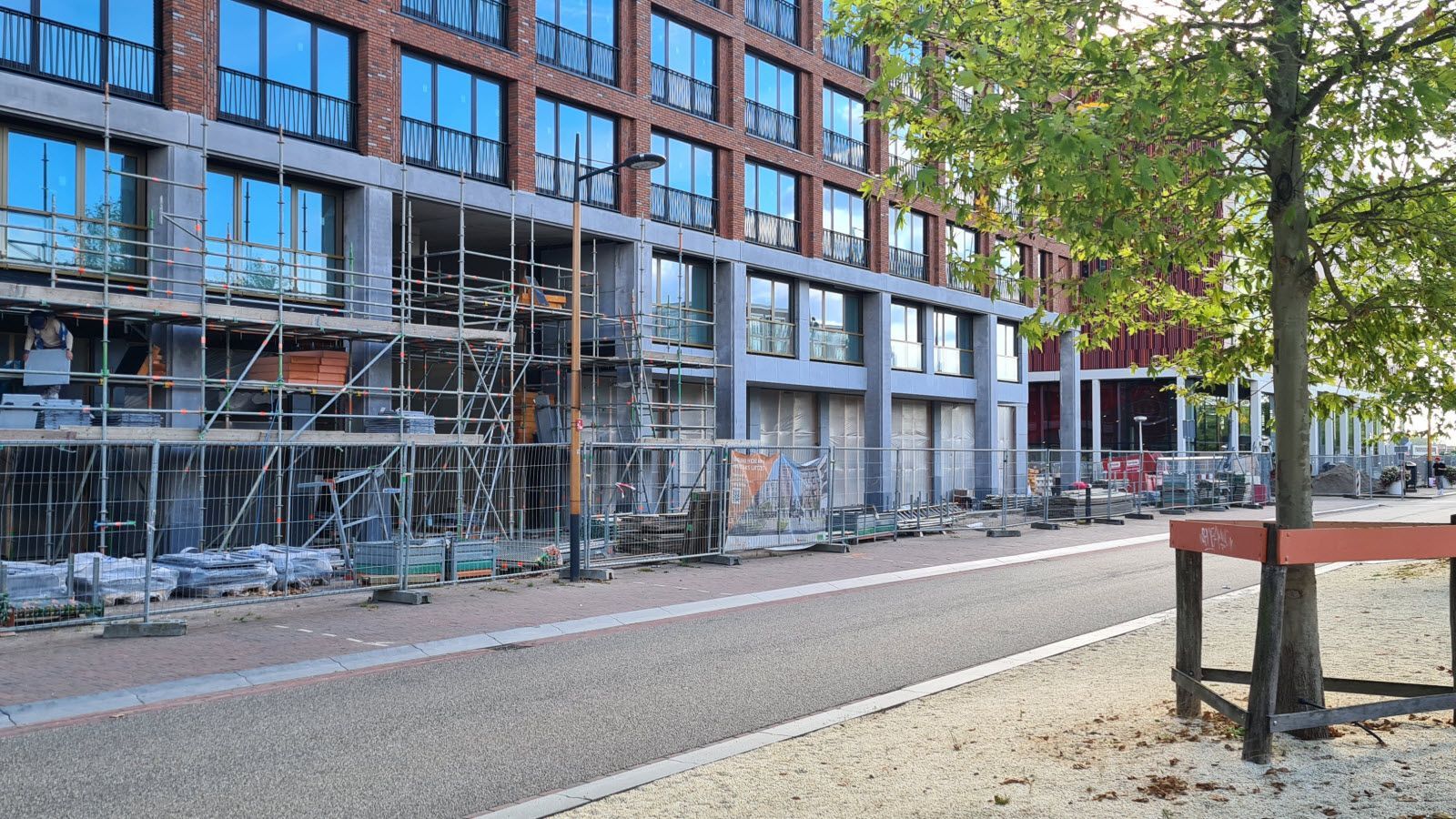 Een groot gebouw in aanbouw met steigers en een boom ervoor.