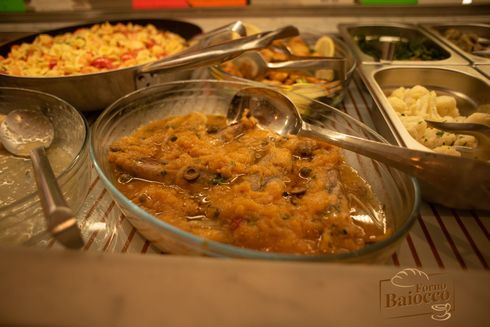 Un buffet con una ciotola di pesce in salsa, una teglia di riso giallo e contorni in contenitori di metallo.