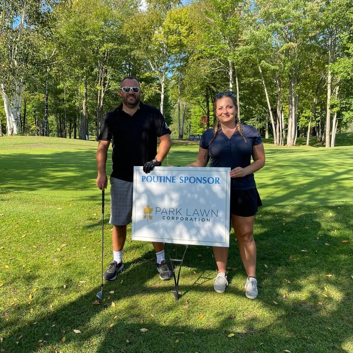 Two team members standing with the Parklawn sponsorship sign at the 2023 Holes for Hospice Golf Tournament