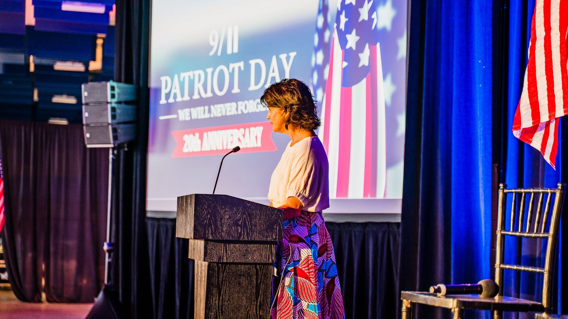 A woman is standing at a podium giving a speech for patriot day.