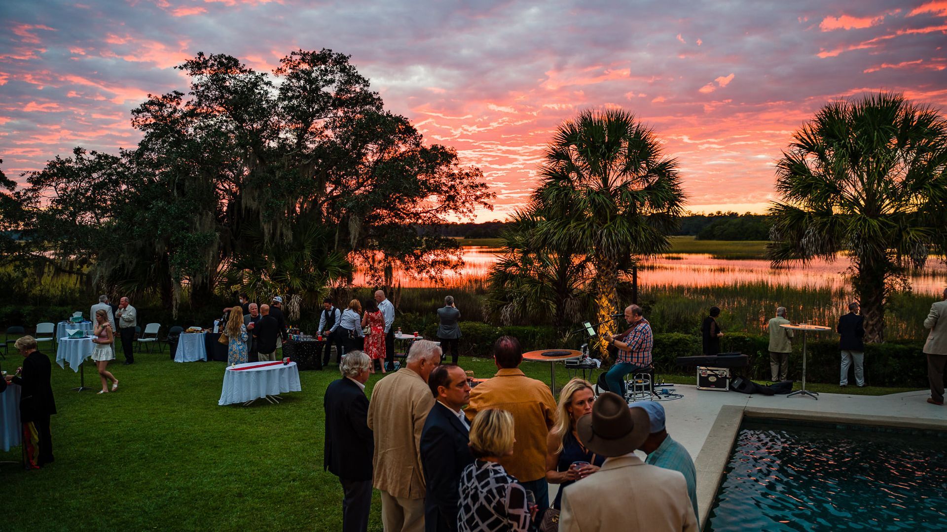 A group of people are standing around a pool at sunset.