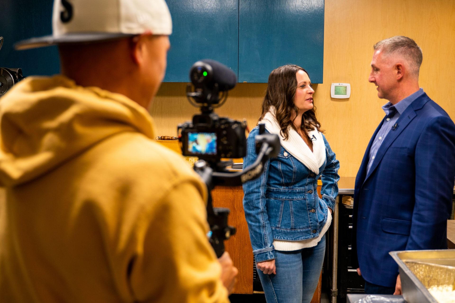 A man is recording a woman and a man in a kitchen.