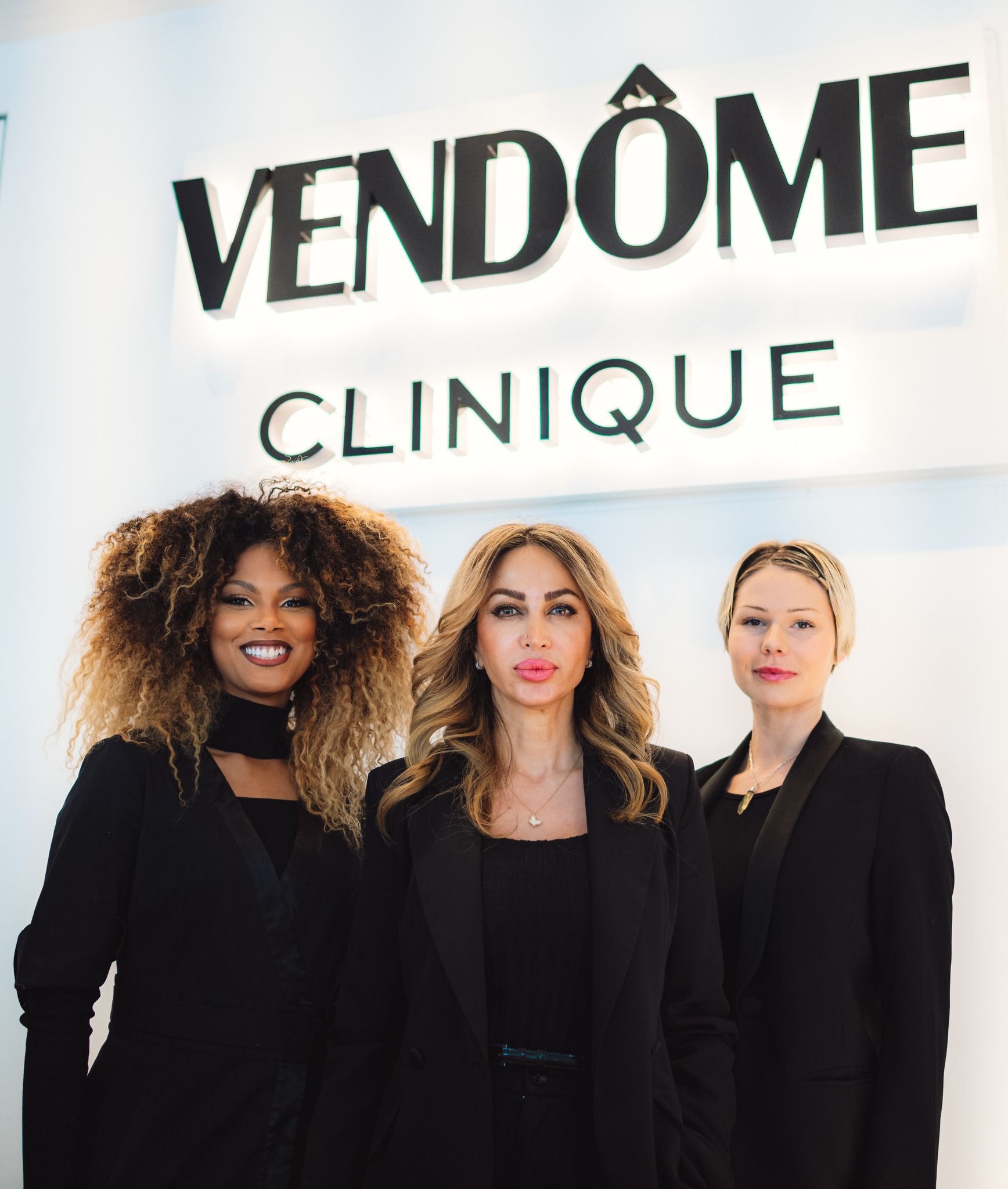 Three women are posing for a picture in front of a vendôme clinique sign.