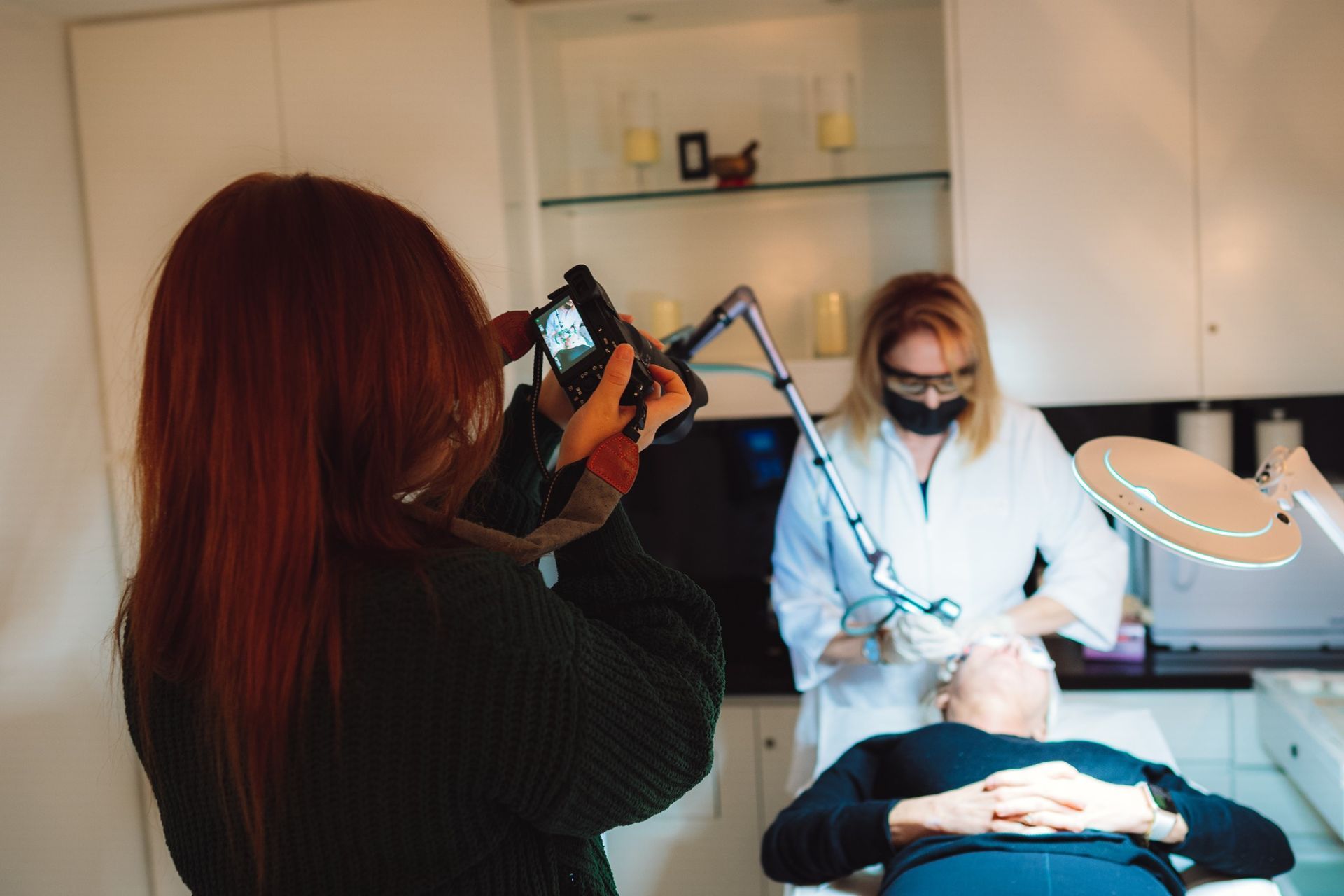 A woman is taking a picture of a man getting a laser treatment.