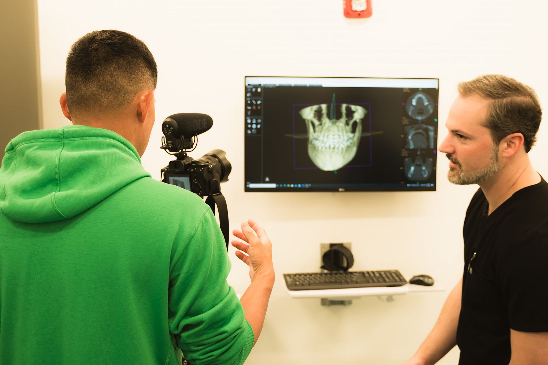 A man in a green hoodie is standing next to a man in a black shirt.