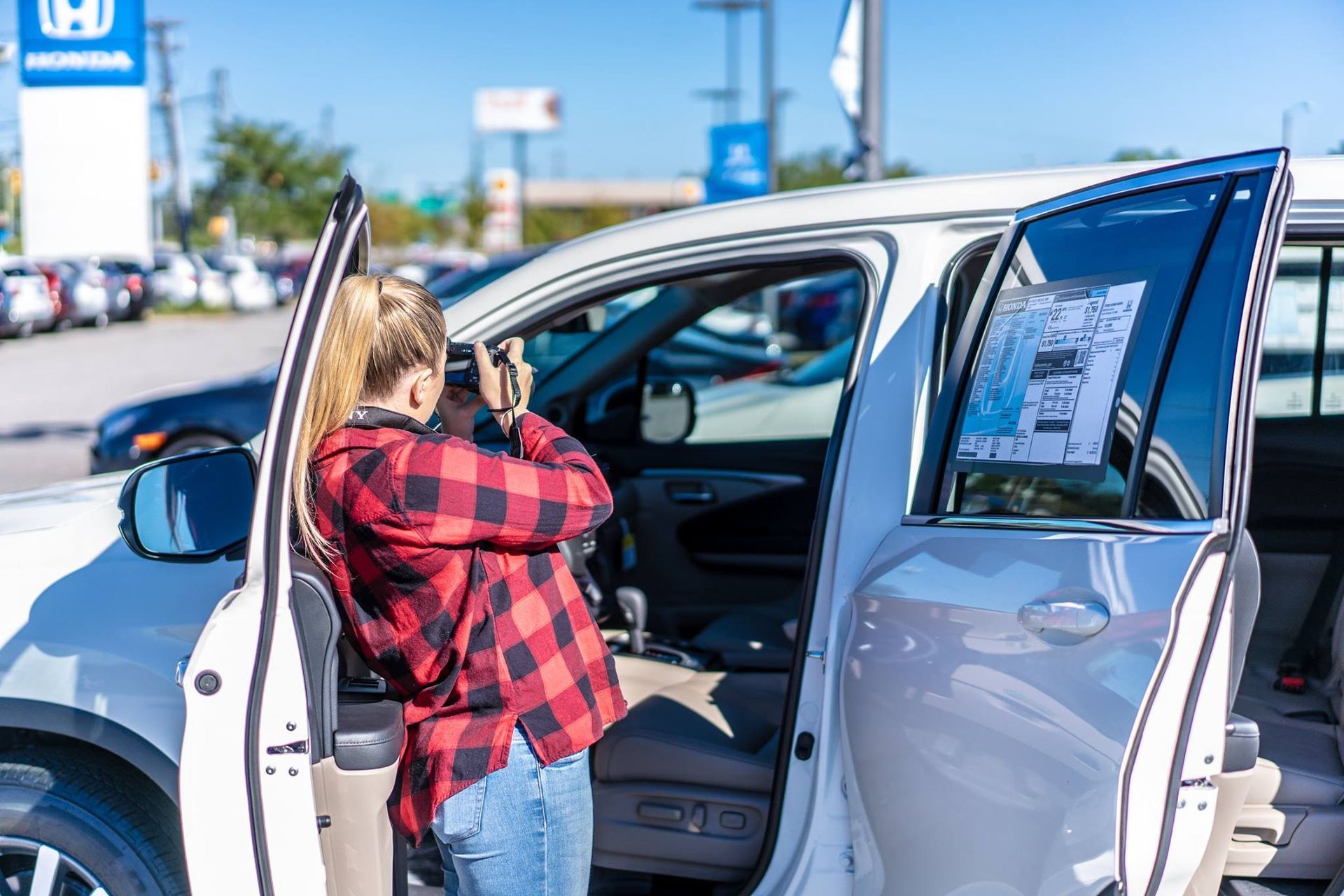 A woman is taking a picture of a car at a car dealership.