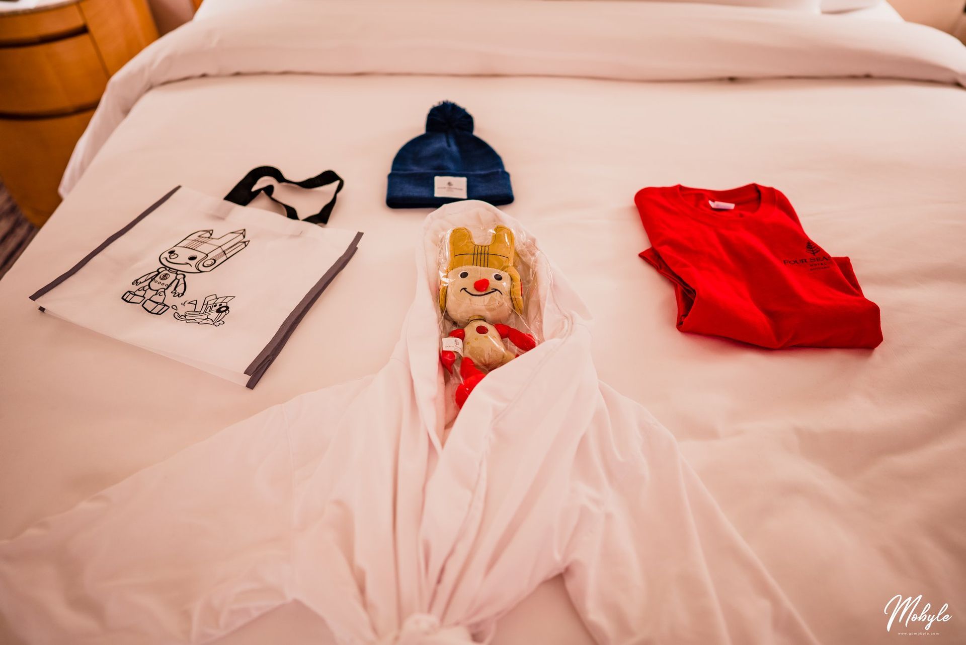 A stuffed animal is wrapped in a white towel on a bed.