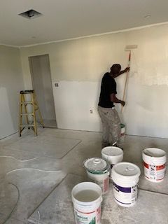 A man is painting a wall in a room with buckets of paint.