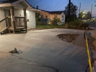 A concrete driveway with a hole in it in front of a house.