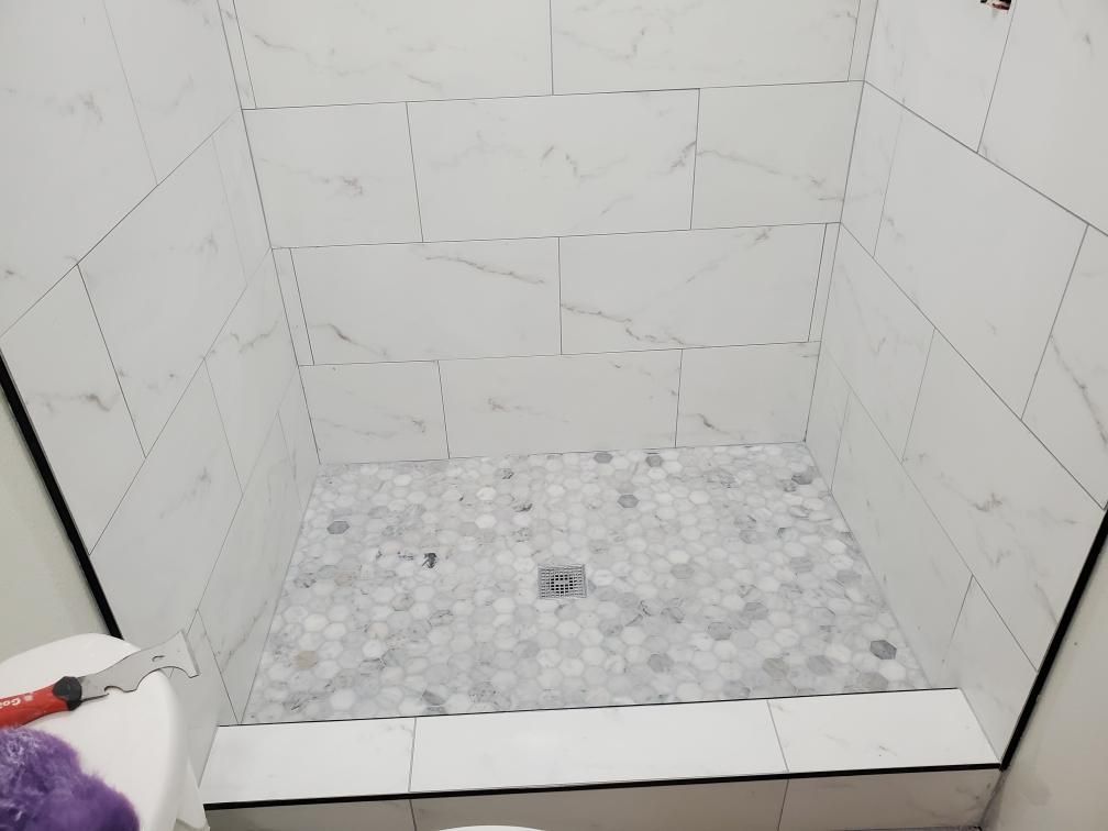 A shower stall with white tiles being installed in a bathroom.