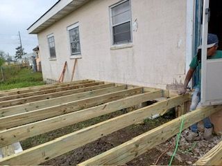 A man is working on a wooden deck in front of a house.