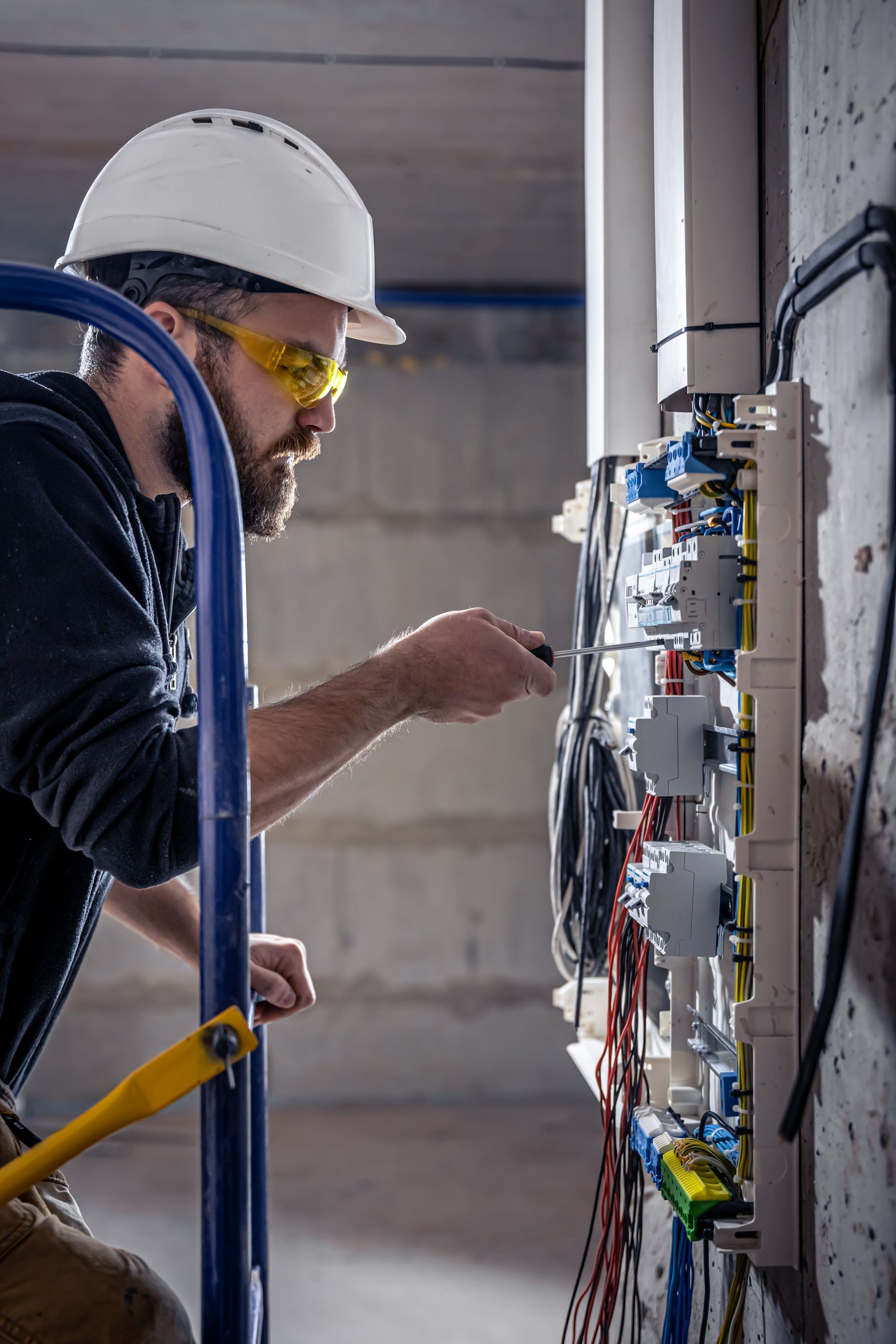 An electrician is working on an electrical box with a screwdriver.