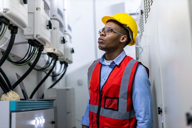 A man wearing a hard hat and safety vest is standing in a room looking up.