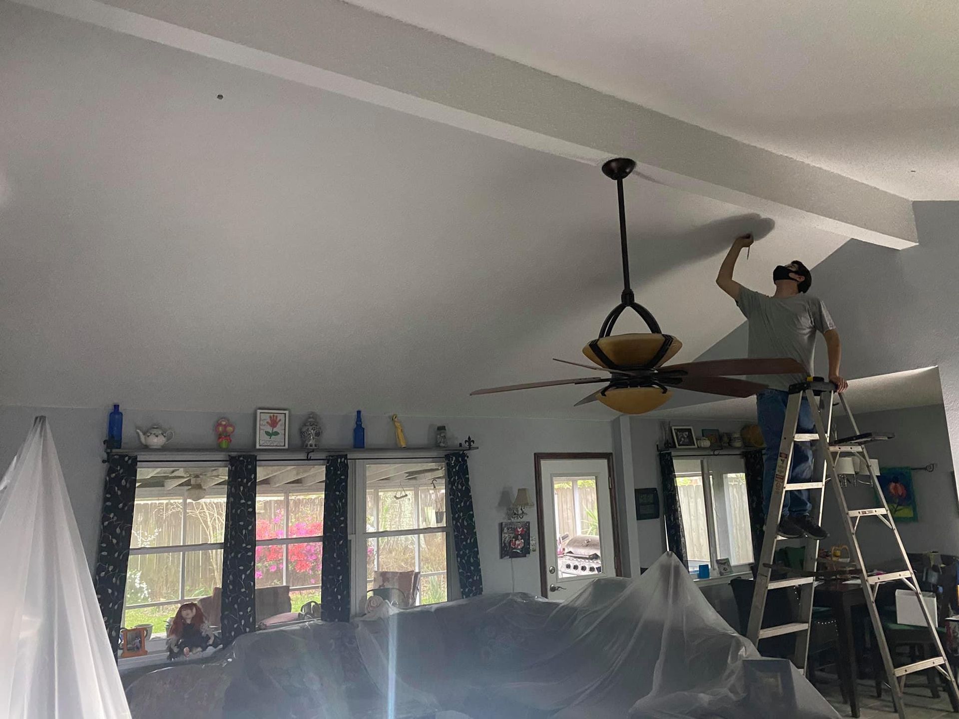A man is painting a ceiling fan in a living room.
