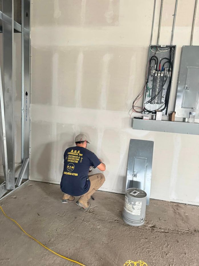 A man is kneeling down in a room while working on a wall.