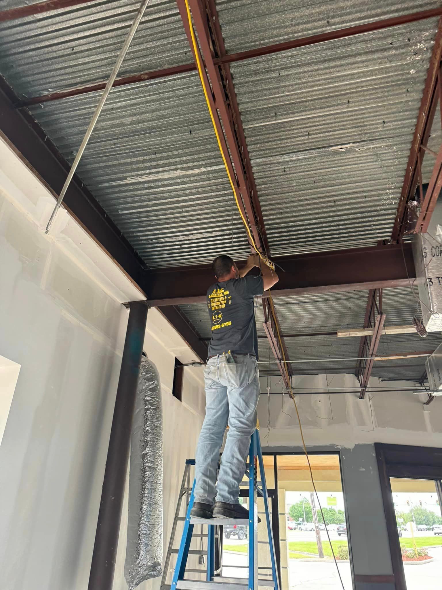 A man is standing on a ladder working on the ceiling of a building.