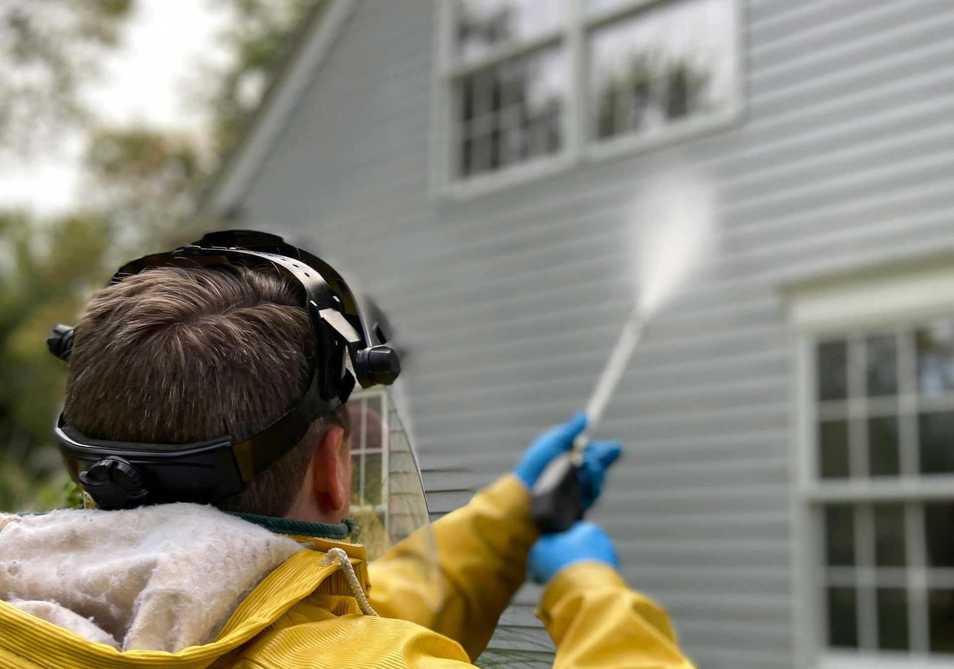 A man in a yellow jacket is cleaning a house with a high pressure washer.