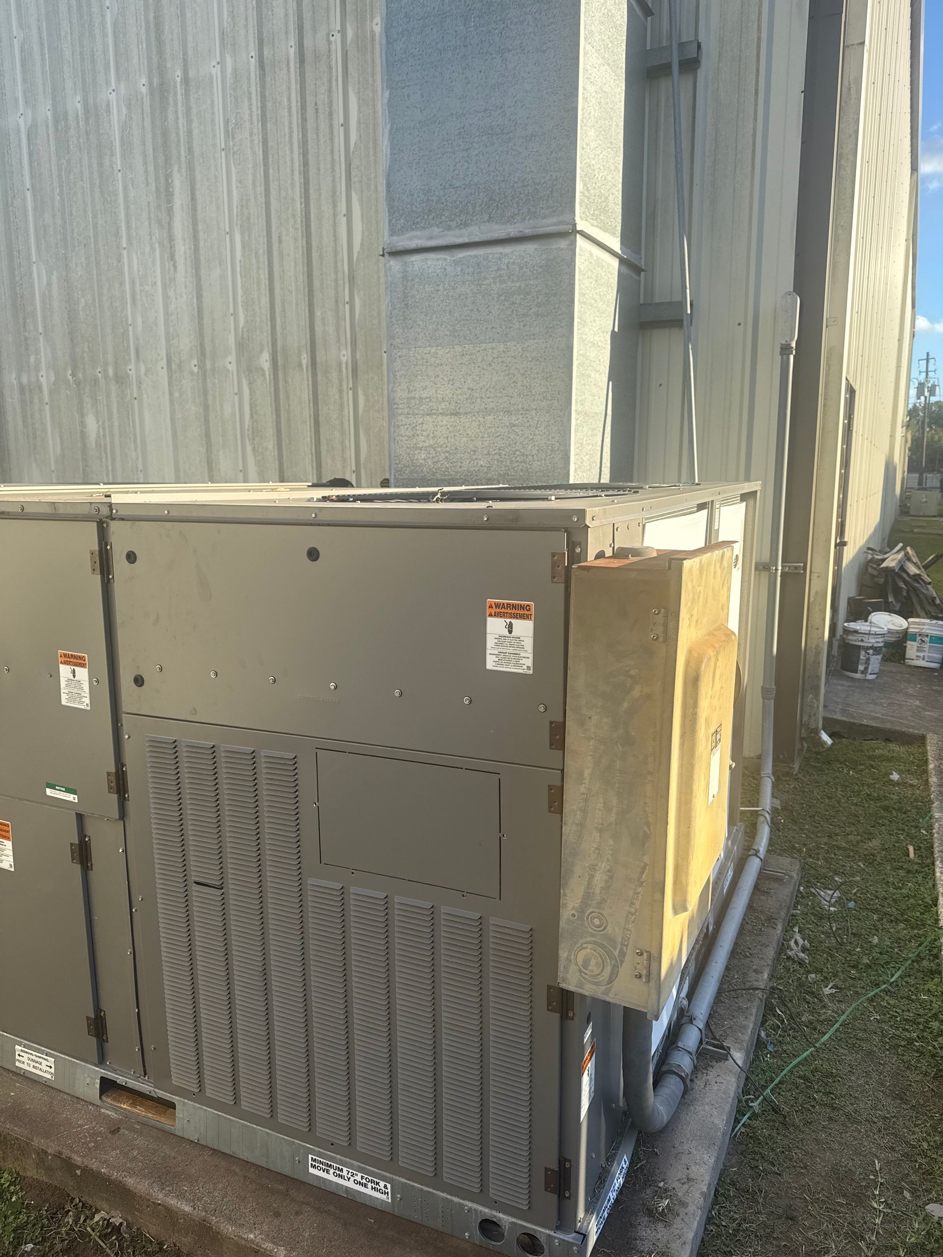 Man in work clothes explaining a heat pump to a couple outdoors near a house.