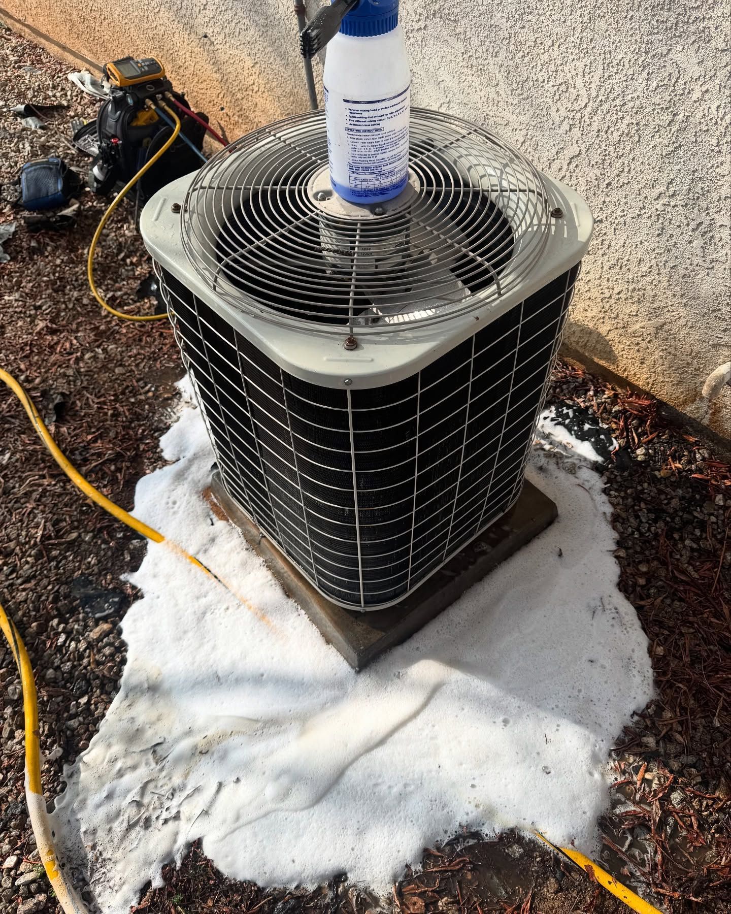 AC unit being cleaned, surrounded by white foam, near a building.
