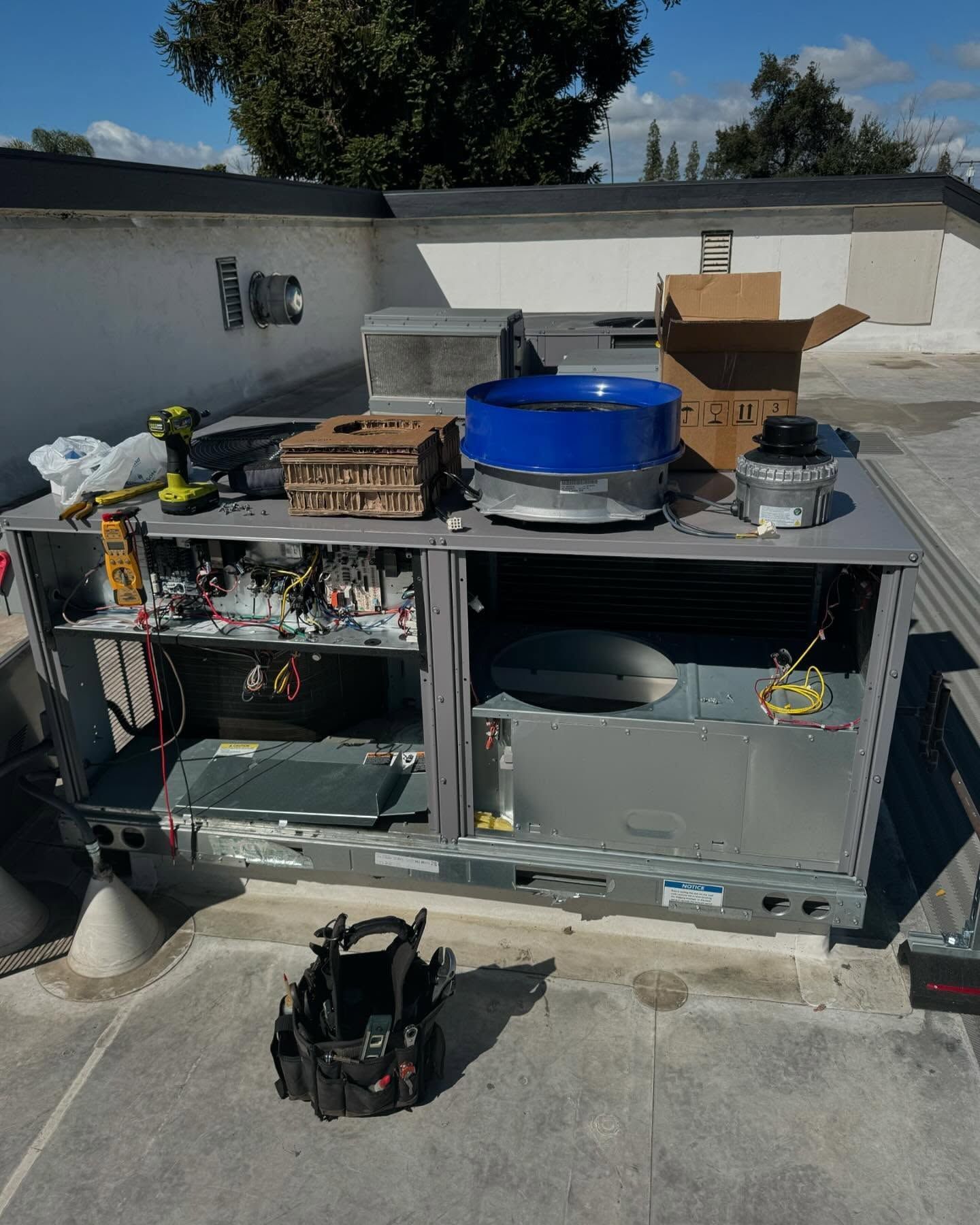 HVAC unit on a rooftop being serviced. Metal, open, with tools and components scattered around. Bright sunny day.